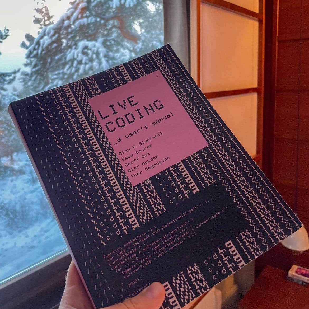 Picture of the book "Live Coding, A user's manual" taken indoor with a window with snowy trees outside.